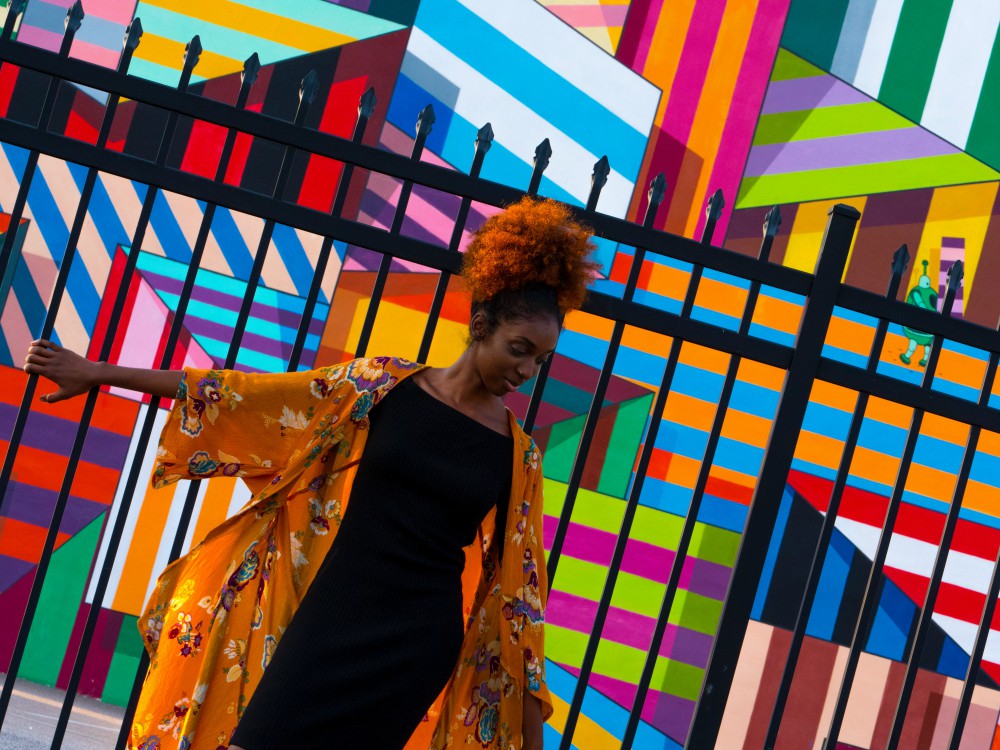 Centered. African-American woman leaning against a fence. Colorful mural