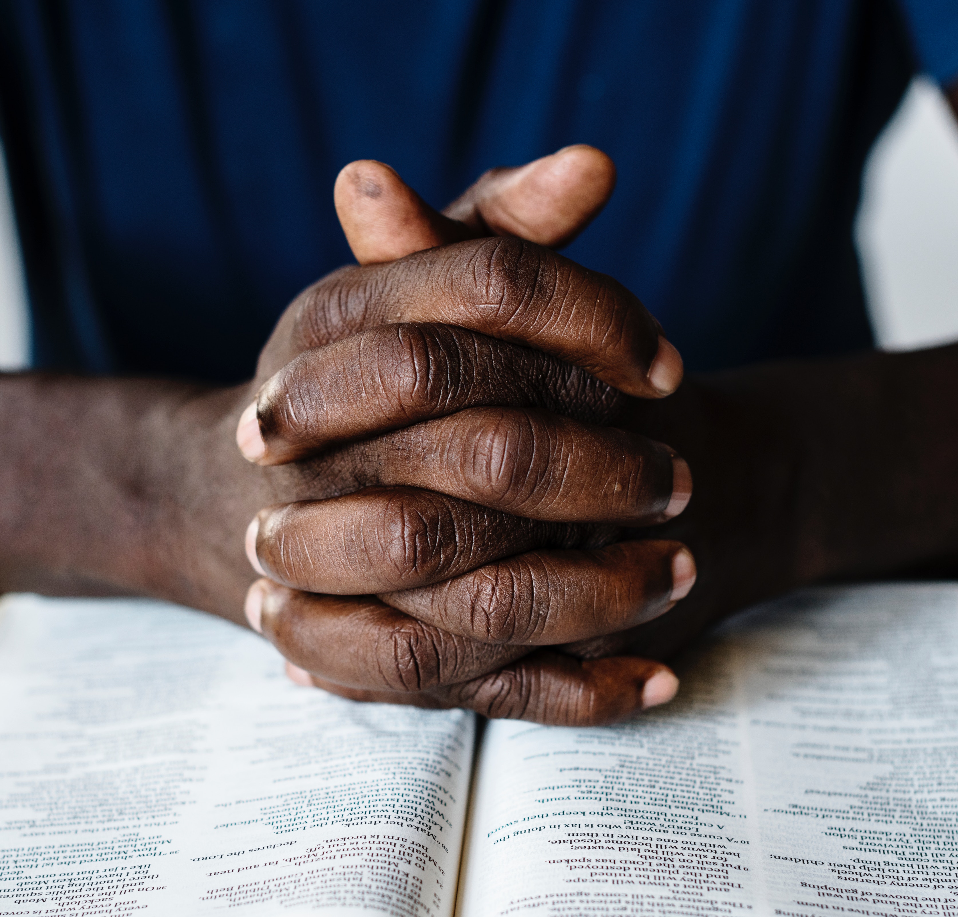hands folded in prayer on top of a Bible