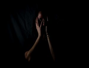 woman in the dark, holding her face